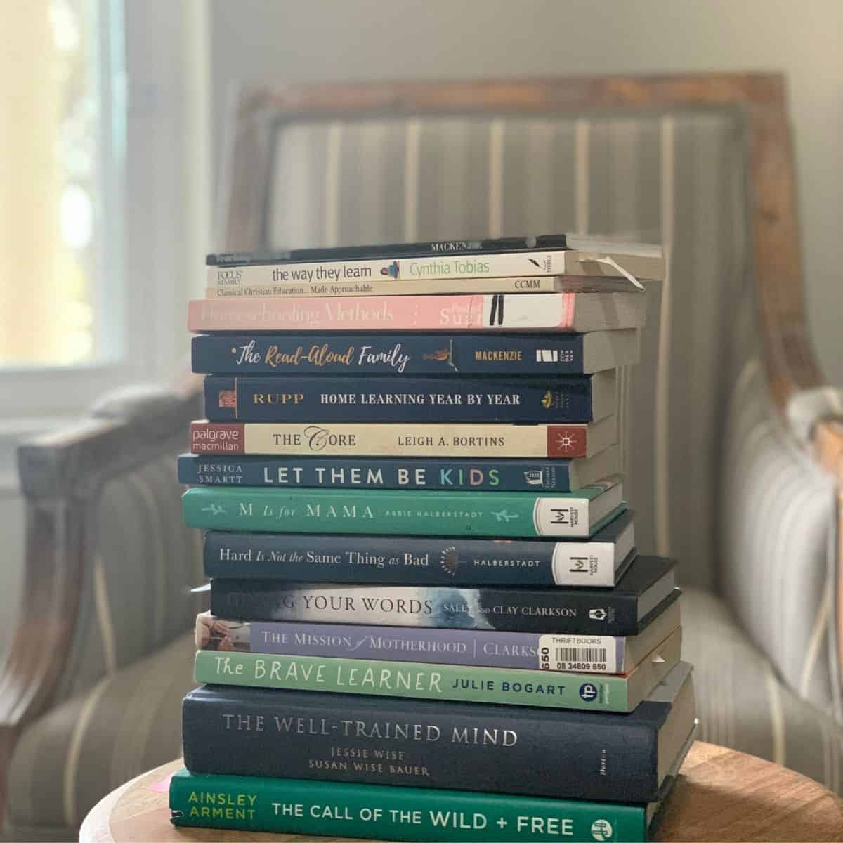 Stack of homeschooling mama books on a table with an open window and chair in the background
